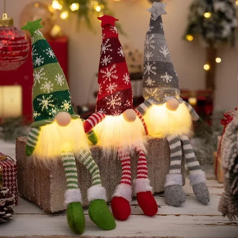 Three glowing Christmas gnomes in red, grey and green sitting on a gift box